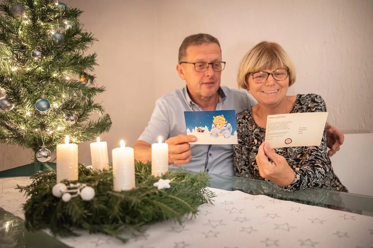 Manželé u adventního věnce se s úsměvem dívají na pohlednici od Ježíška